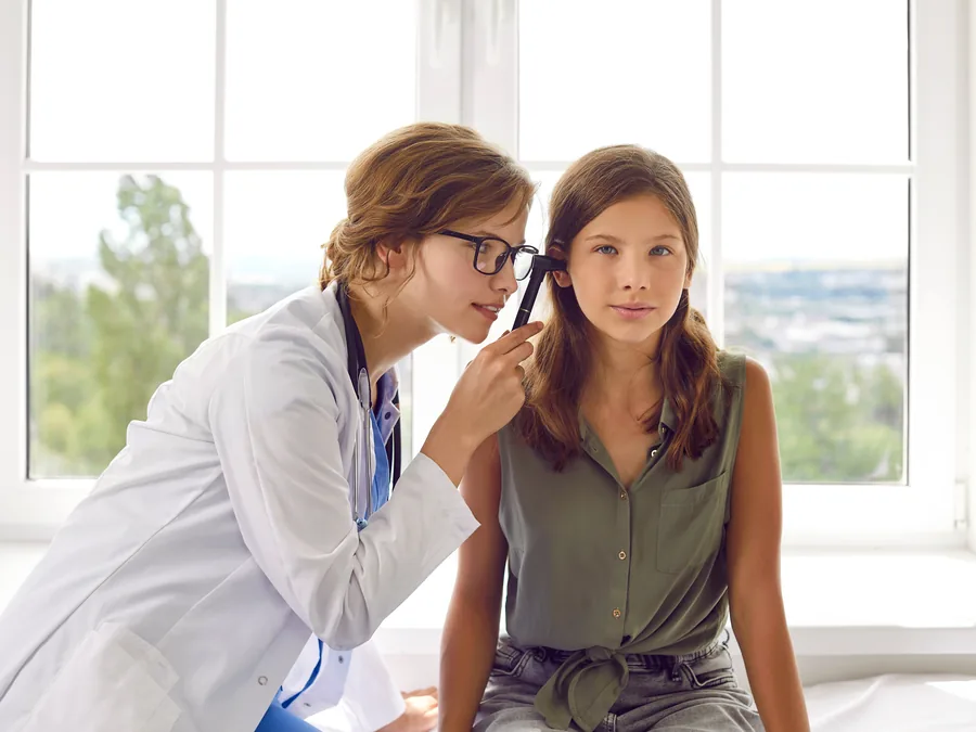 Médica examinando a orelha de uma adolescente em consultório