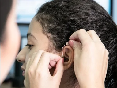 Paciente colocando um aparelho auditivo atrás da orelha